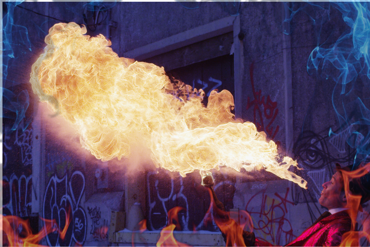 FireGuy blowing a fireball that is as long as he is tall nearly in what appears to be an outdoor stage in front of a graffitied wall.