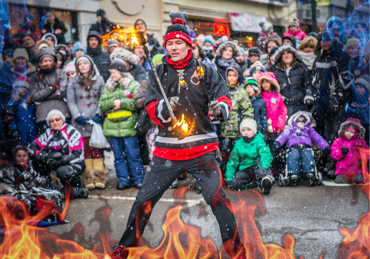 FireGuy juggling a fiery baton during a snowy day for a crowd during a street show with additional flames on image for added affect.