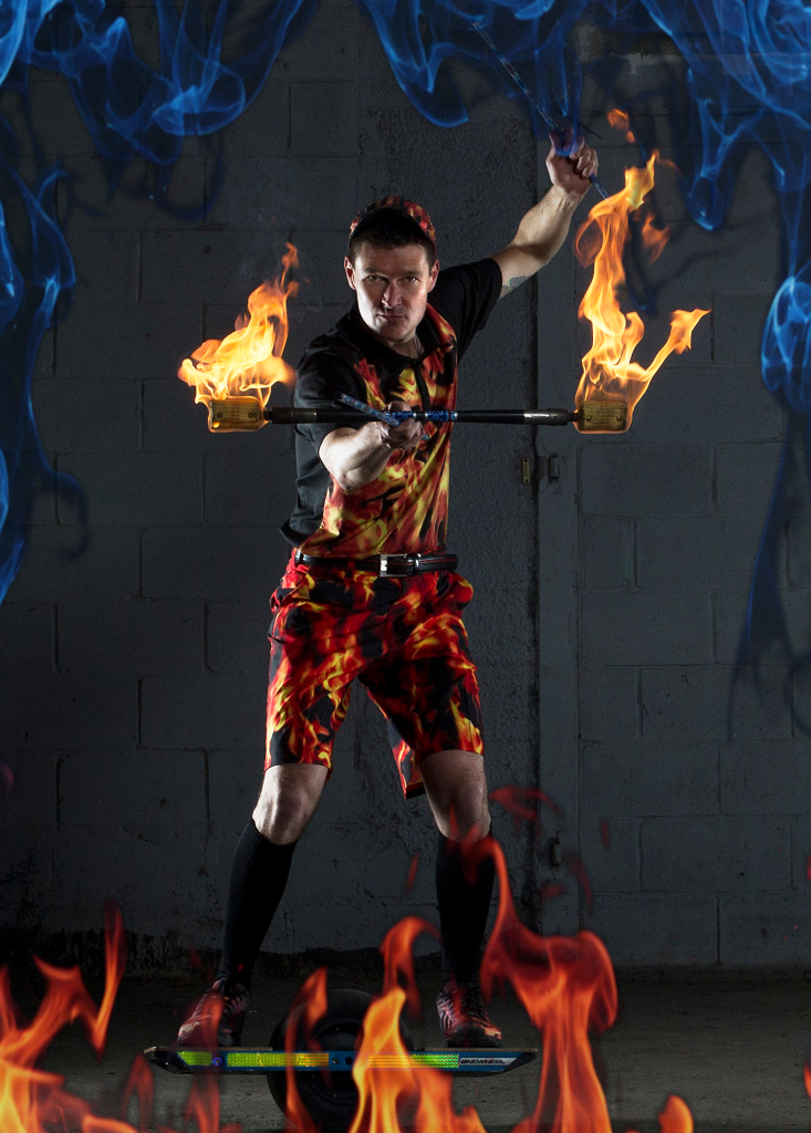 FireGuy holding his fiery baton, standing on a one wheeled scooter.