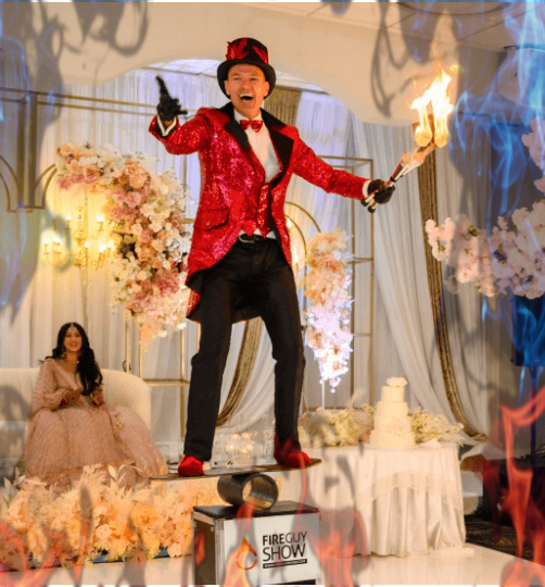 FireGuy standing on a plank, on a pipe, on a box and holding 2 of his juggling fire sticks inside at a wedding reception.