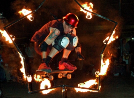 FireGuy jumping through a fiery star shaped hoop on a sakteboard as part of his show.