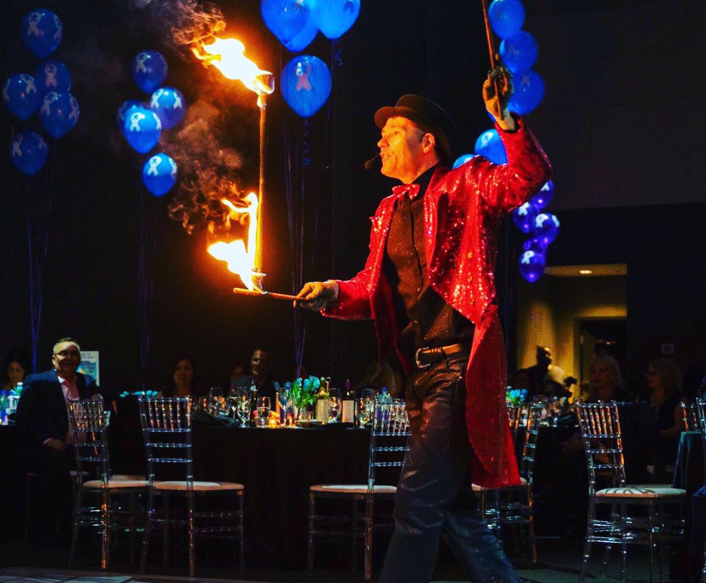 FireGuy walking through a room balancing his fire baton on fire.